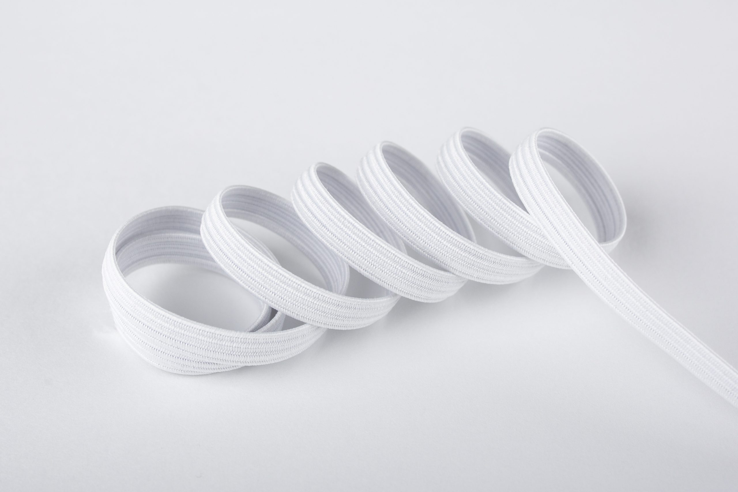 Primer plano de cinta elástica de trencilla blanca con textura visible, elasticidad y alta resistencia.